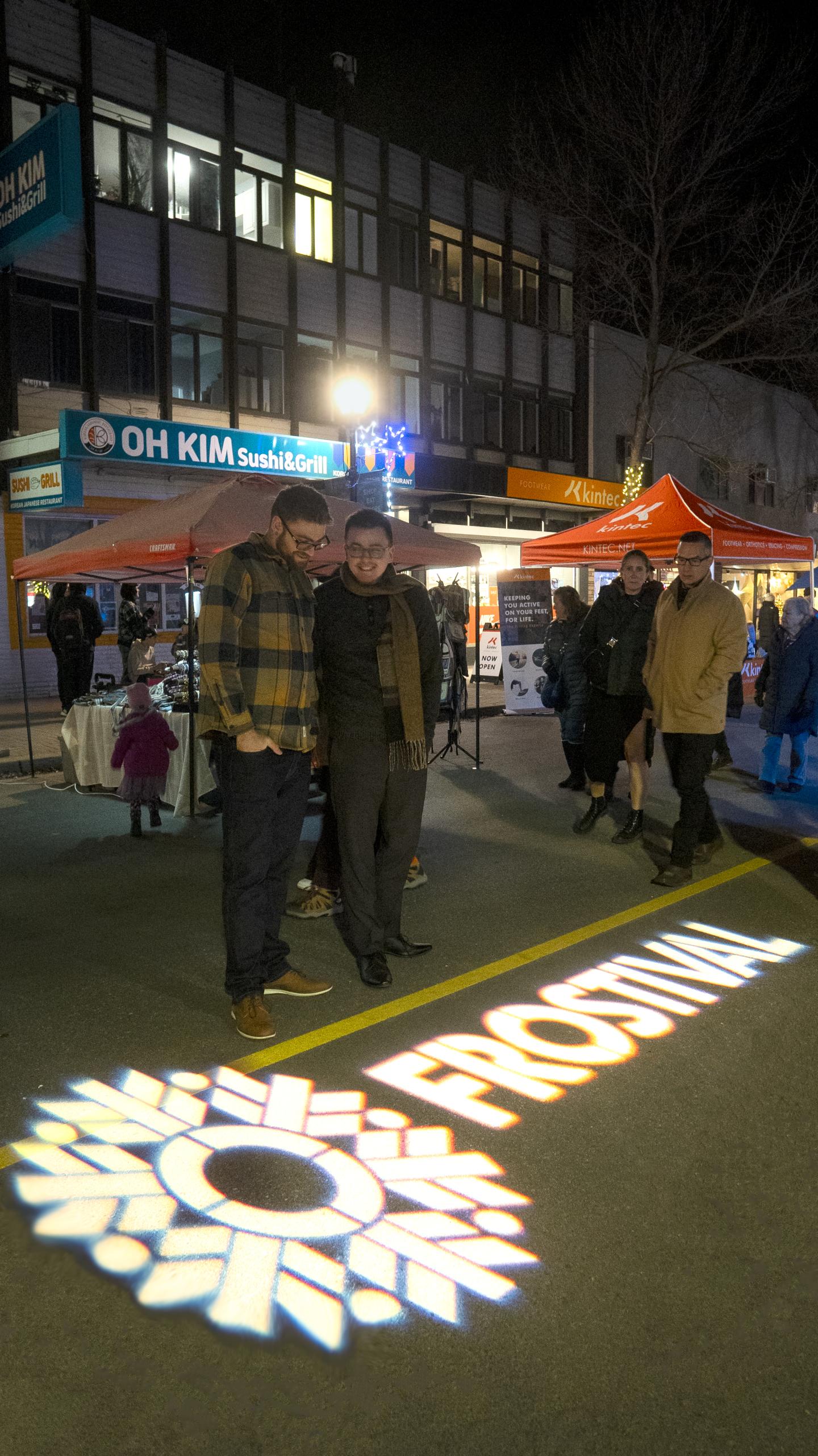 Street festival at night with people, colorful lights, and outdoor stalls.