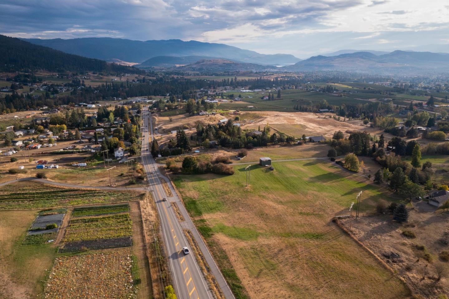 Aerial view of a rural landscape with fields, road, and distant mountains under a cloudy sky.