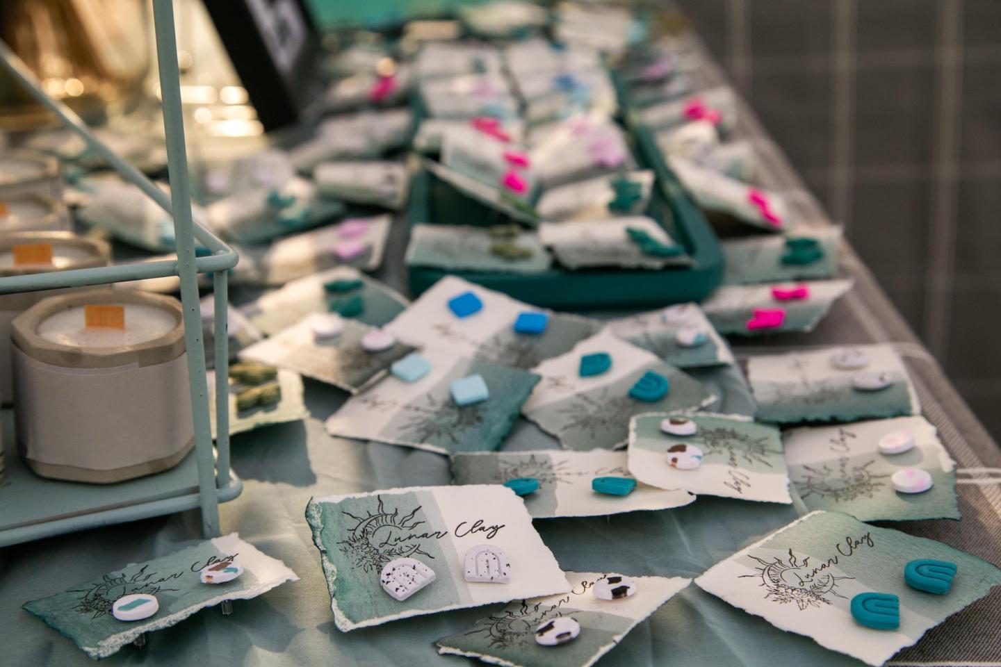 Assorted earrings on display at a market stall with pastel colors and candles nearby.