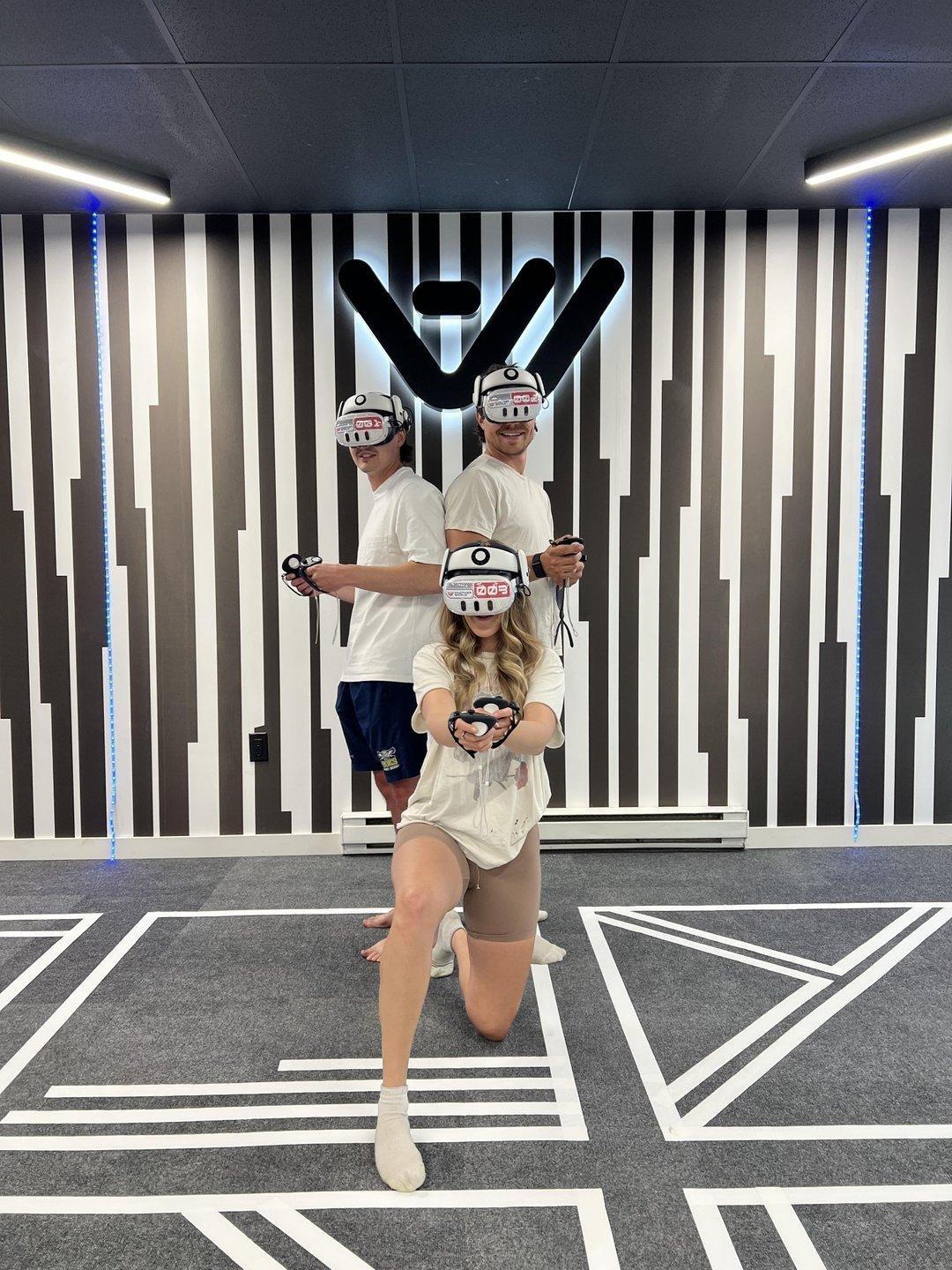 Three people wearing VR headsets pose in a modern room with striped walls.