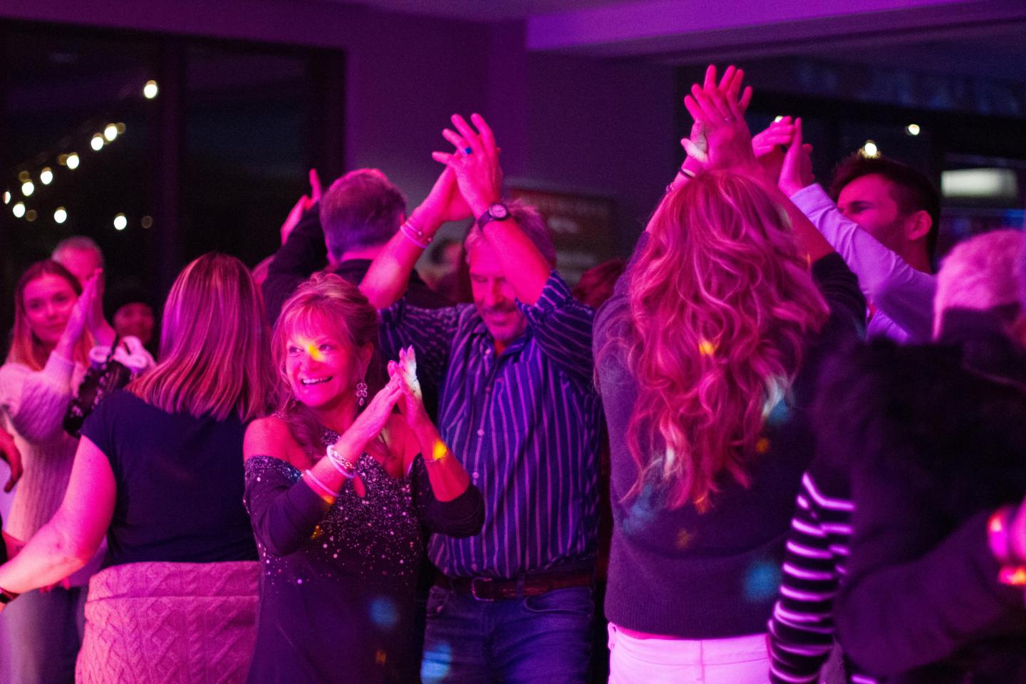 A group of people dancing together under vibrant purple and pink stage lights at the Parka Party.