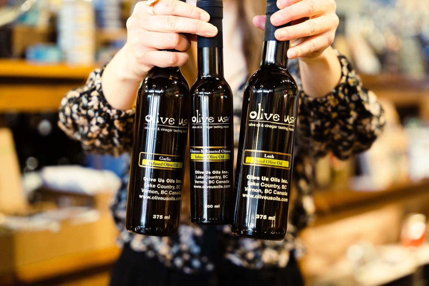 Three bottles of olive oil held by a person in a store.
