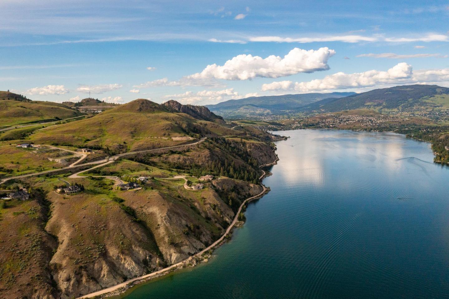 Aerial view of a serene lake with surrounding hills under a blue sky with clouds.