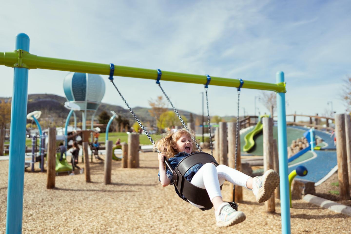 Child joyfully swinging at a colorful playground on a sunny day.