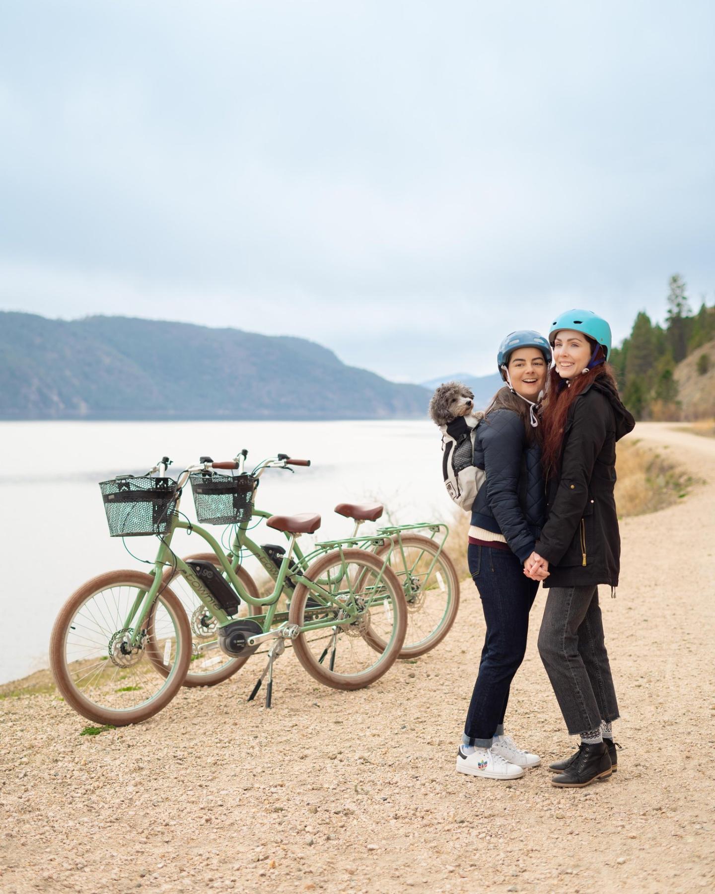 Two people with helmets standing by electric bikes on a lakeside path.
