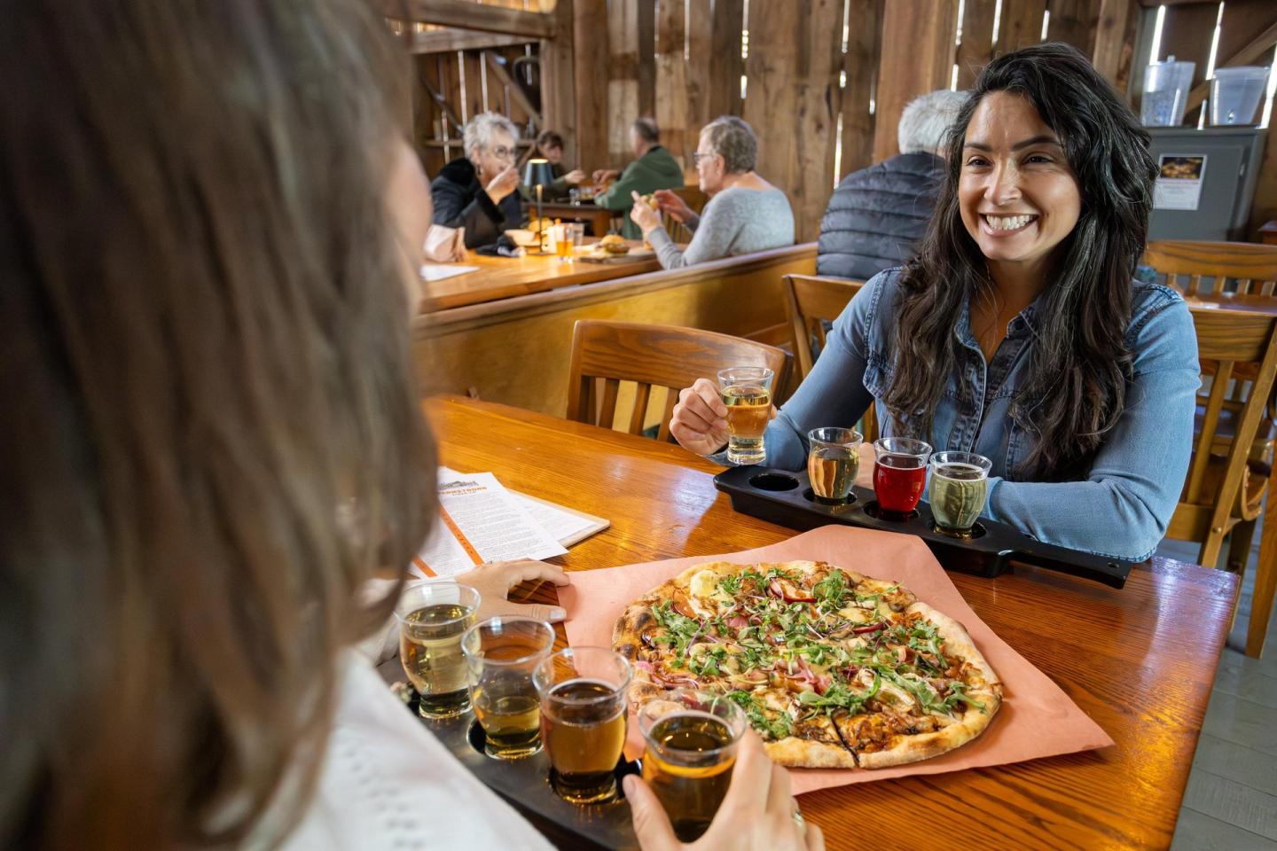 Two people enjoying pizza and drinks at a wooden table in a cozy restaurant.