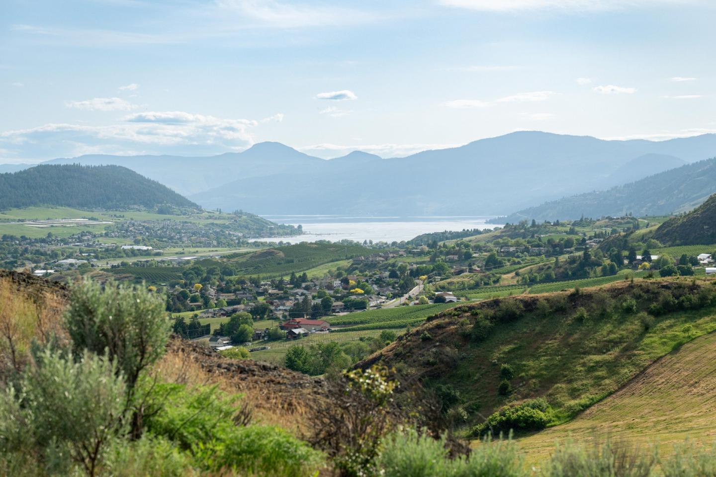 Scenic valley with hills, a lake, and distant mountains under a clear sky.