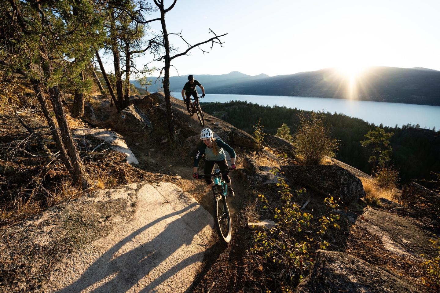 Cyclists on a scenic mountain trail at sunset near a lake.