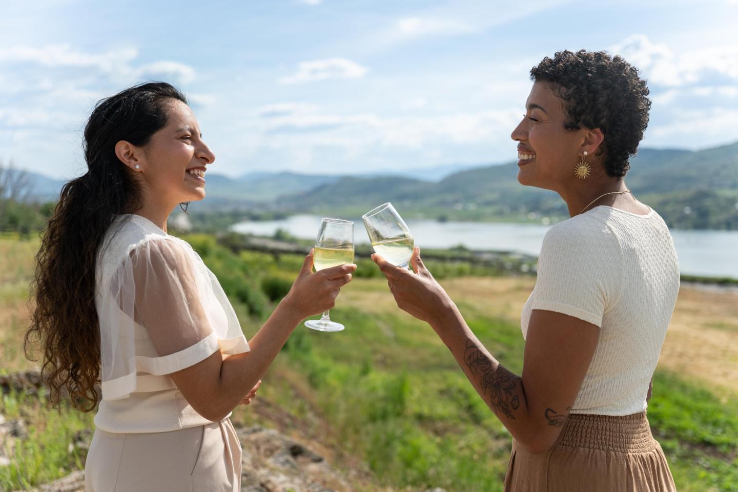 Two women smiling and toasting with wine glasses outdoors.