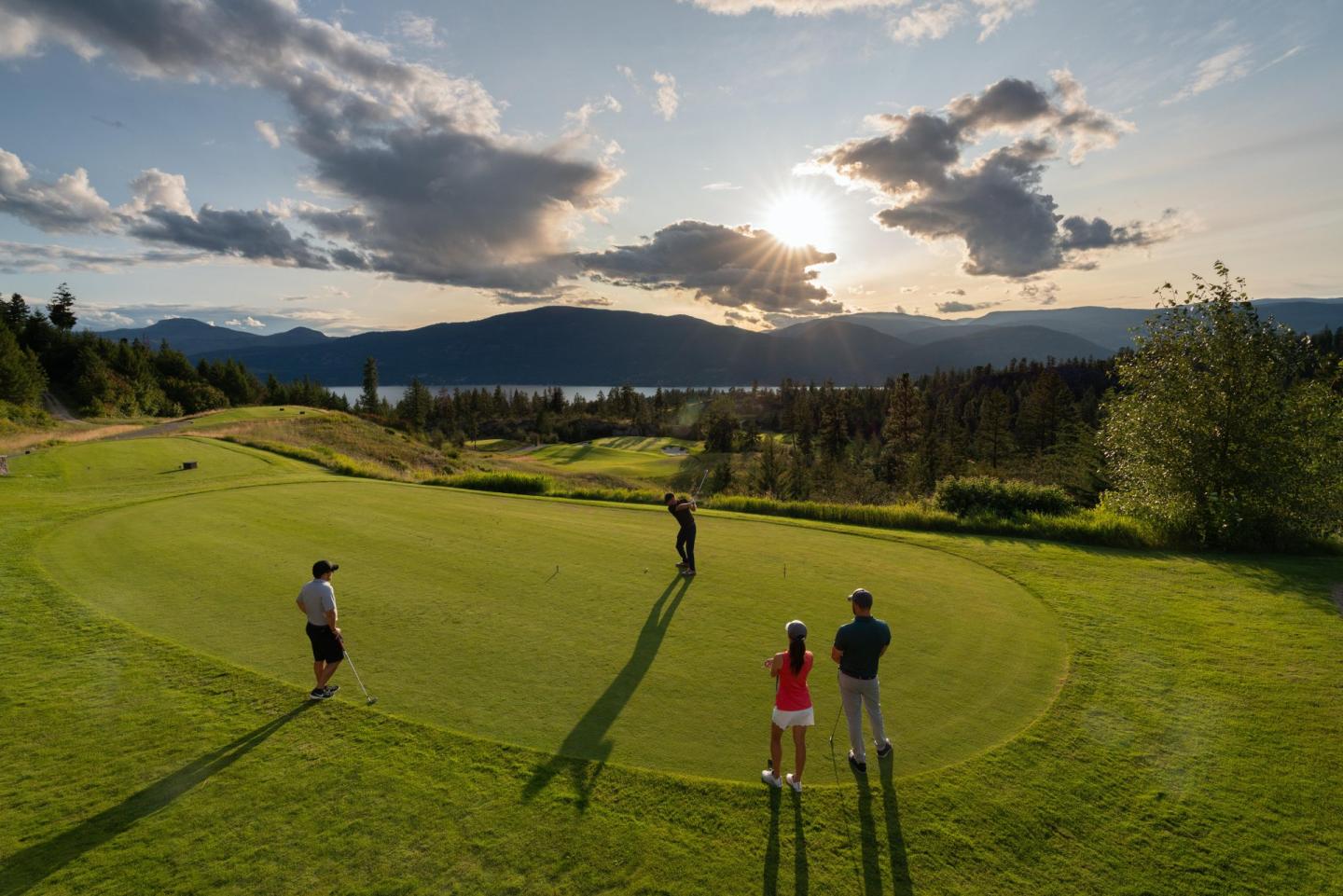 Golfers on a green at sunset, with mountains in the background.