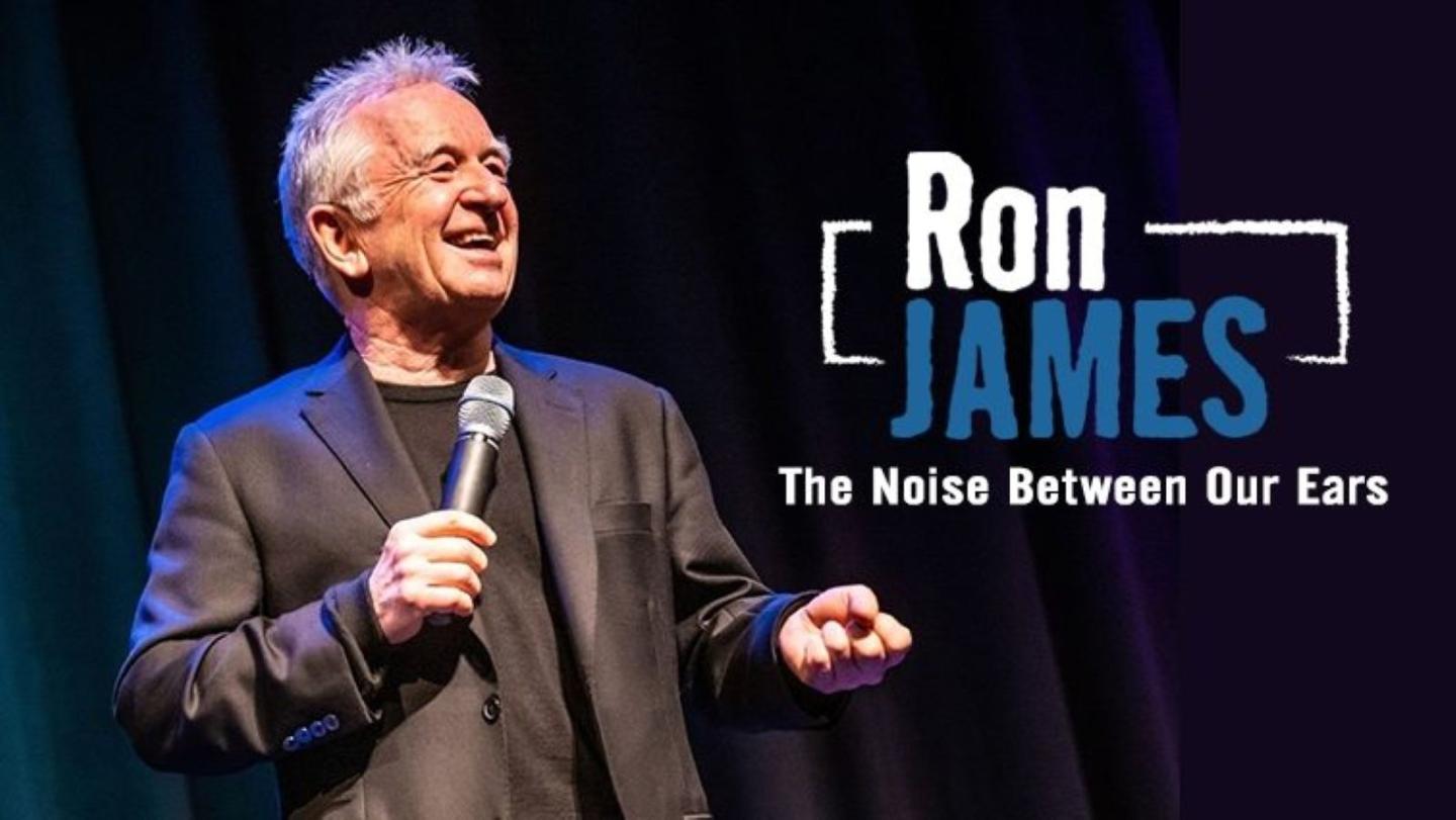 Comedian on stage holding a microphone, backdrop text says "Ron James."