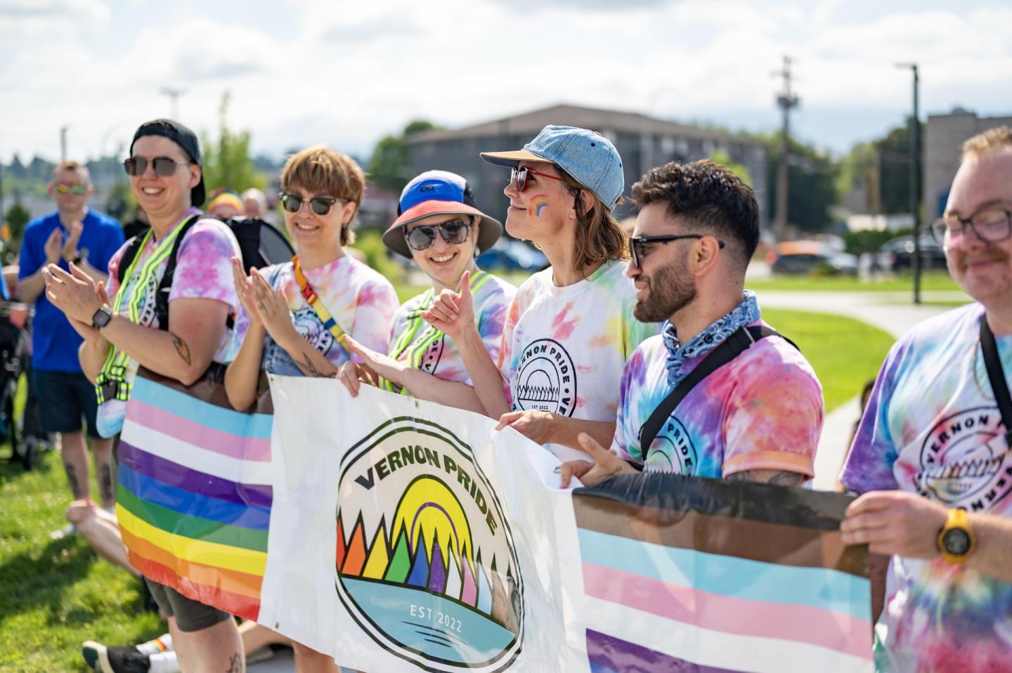 People in colorful shirts holding pride flags, smiling outdoors.