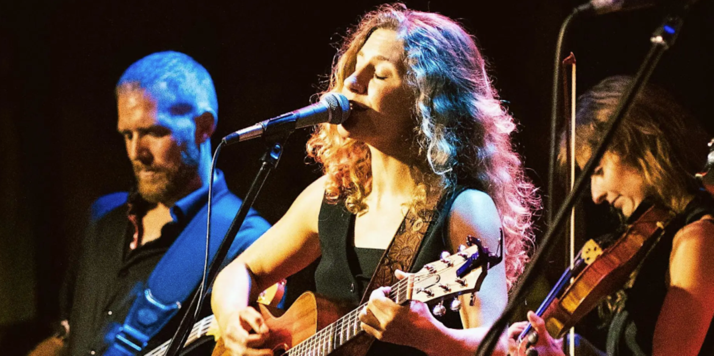 Musicians performing on stage with guitars and a violin.