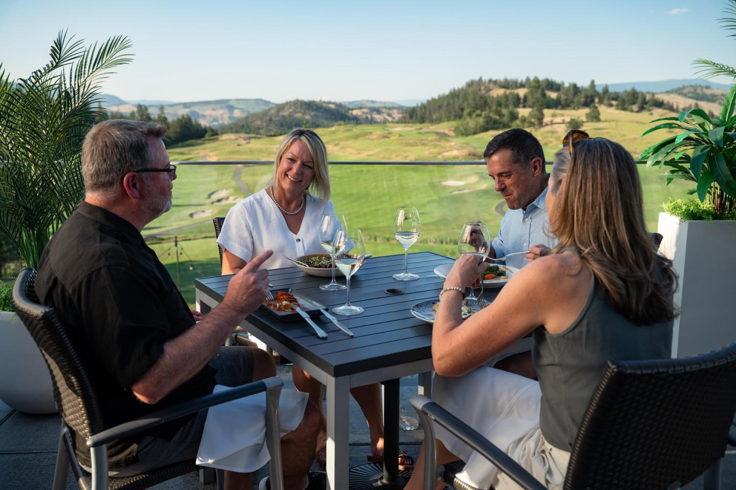 Four people dining outdoors with scenic hills in the background.