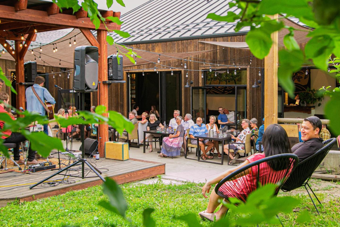Outdoor concert with people seated on chairs, surrounded by greenery.