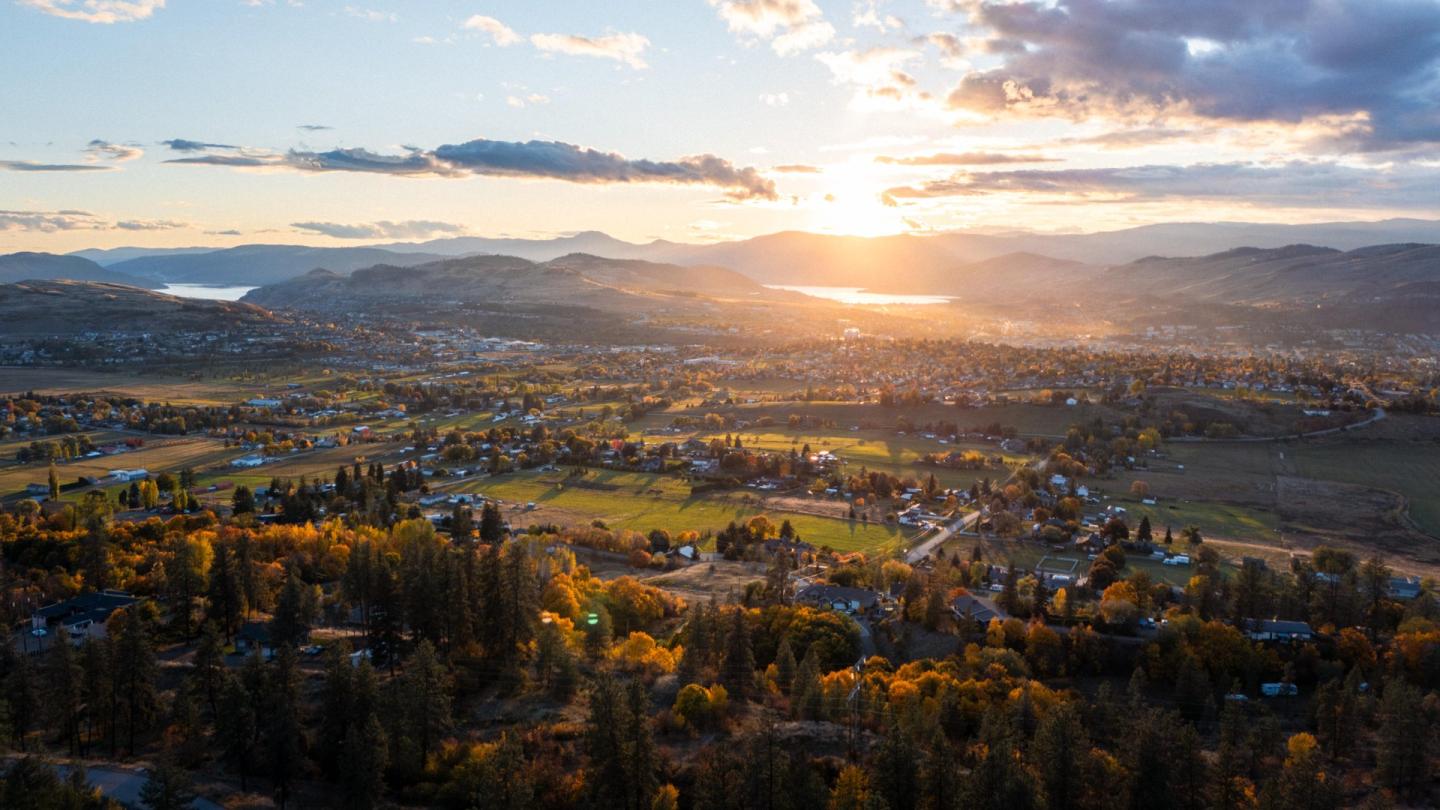 Sunset over a sprawling rural landscape with trees and distant mountains.