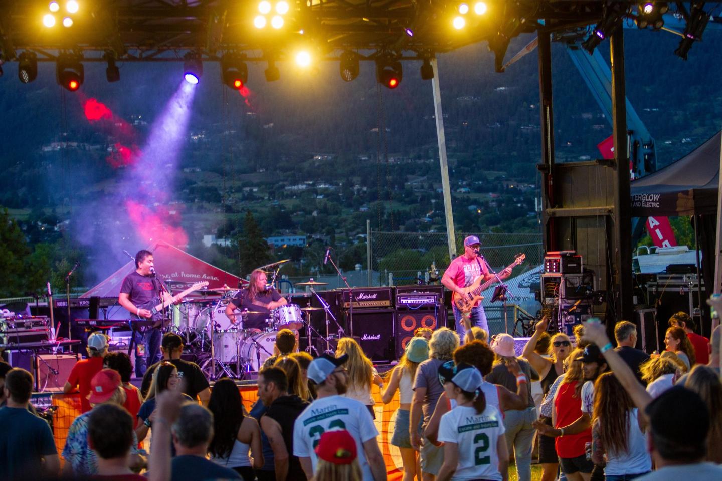 Outdoor concert with a band performing on stage, colorful lights and crowd cheering.