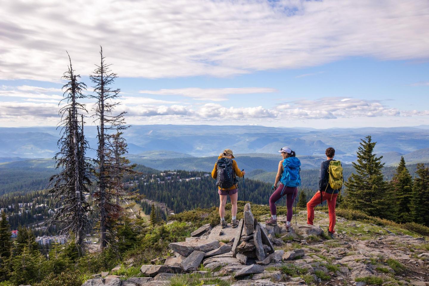 Three hikers admire a scenic mountain view under a cloudy sky.