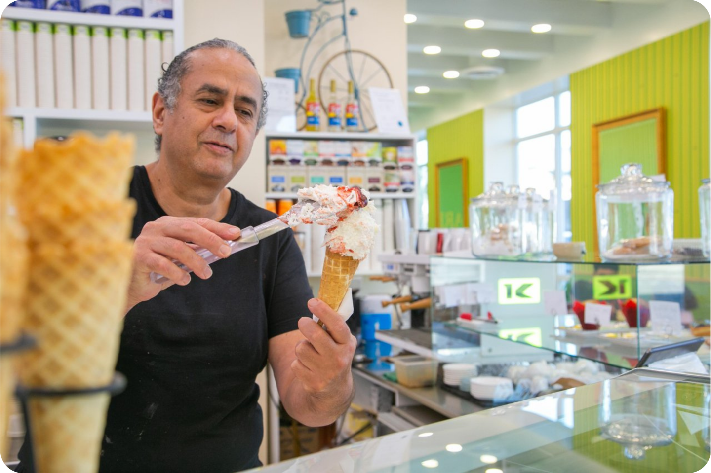 Man serving ice cream cone at a brightly lit shop counter.