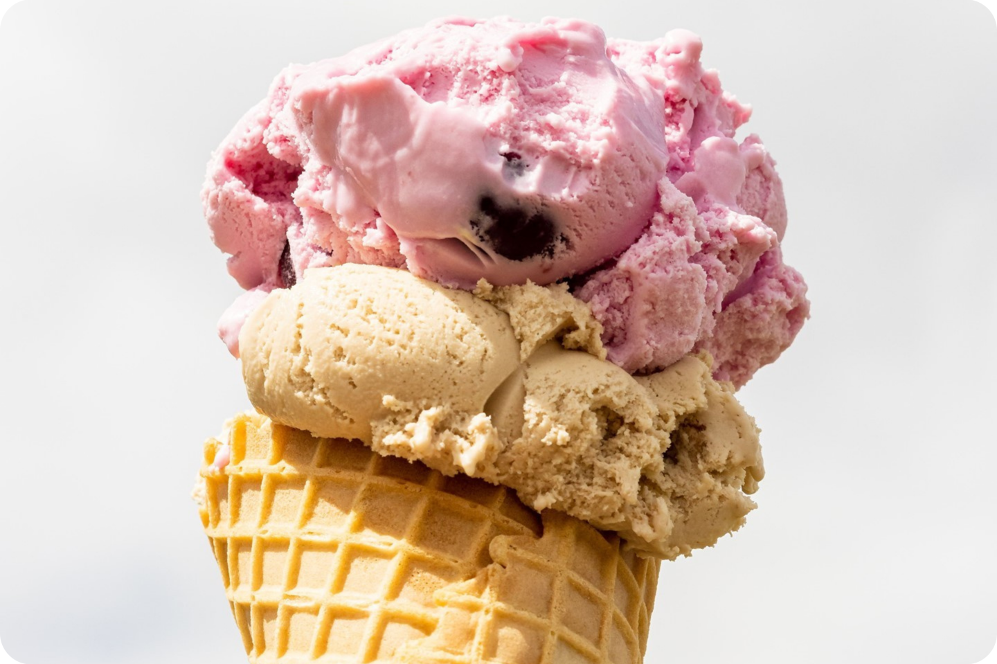 Ice cream cone with pink and beige scoops against a cloudy sky.