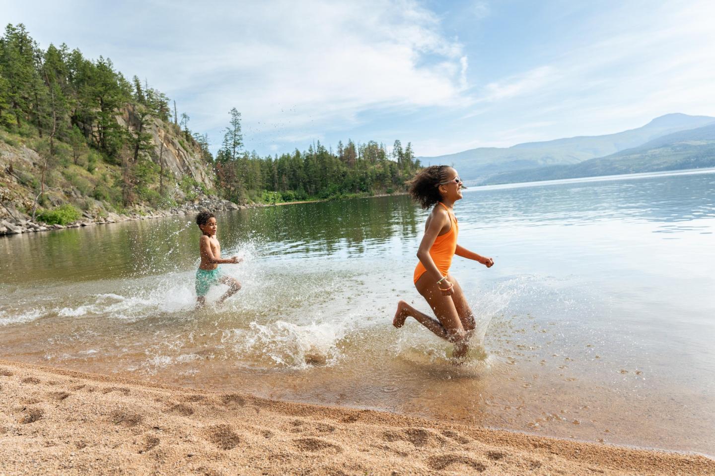 Children joyfully running along a sandy lakeshore.