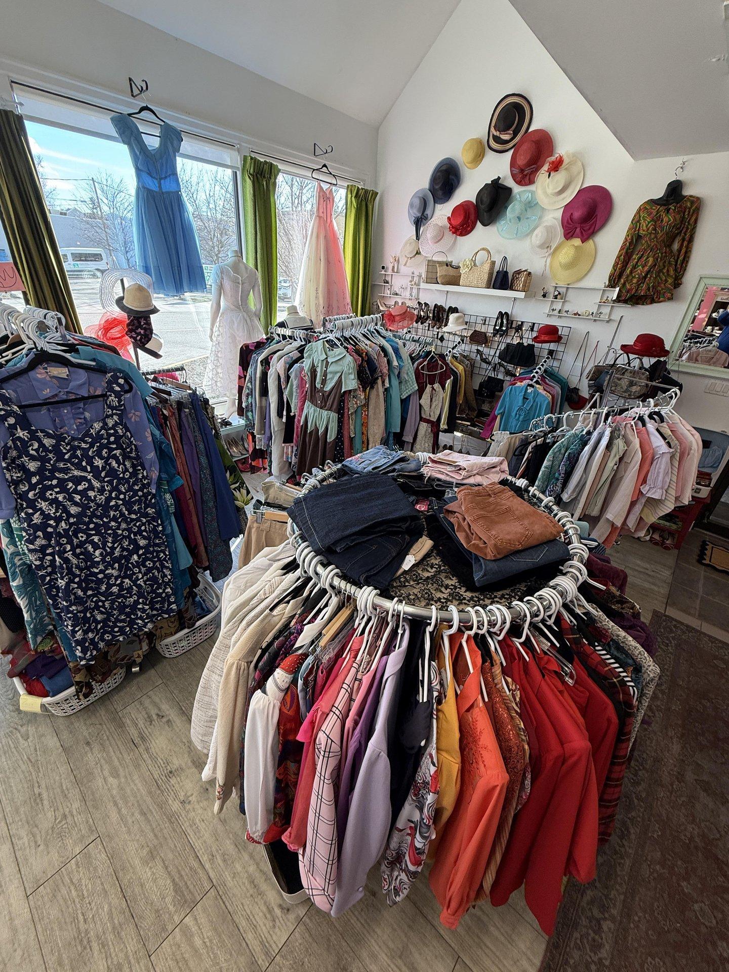 Clothing store with racks of colorful clothes and hats on the wall.