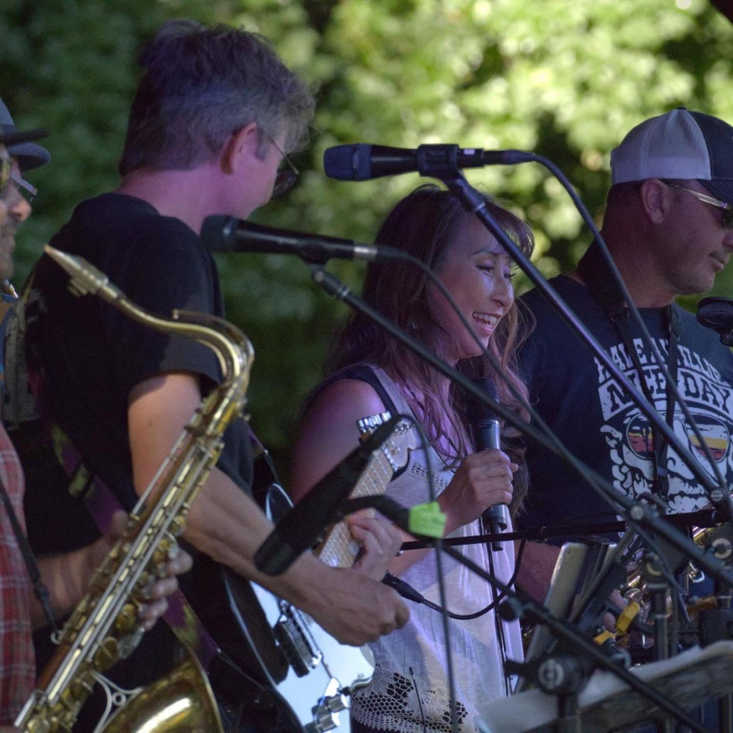 Band performing outdoors, musicians with microphones and instruments.