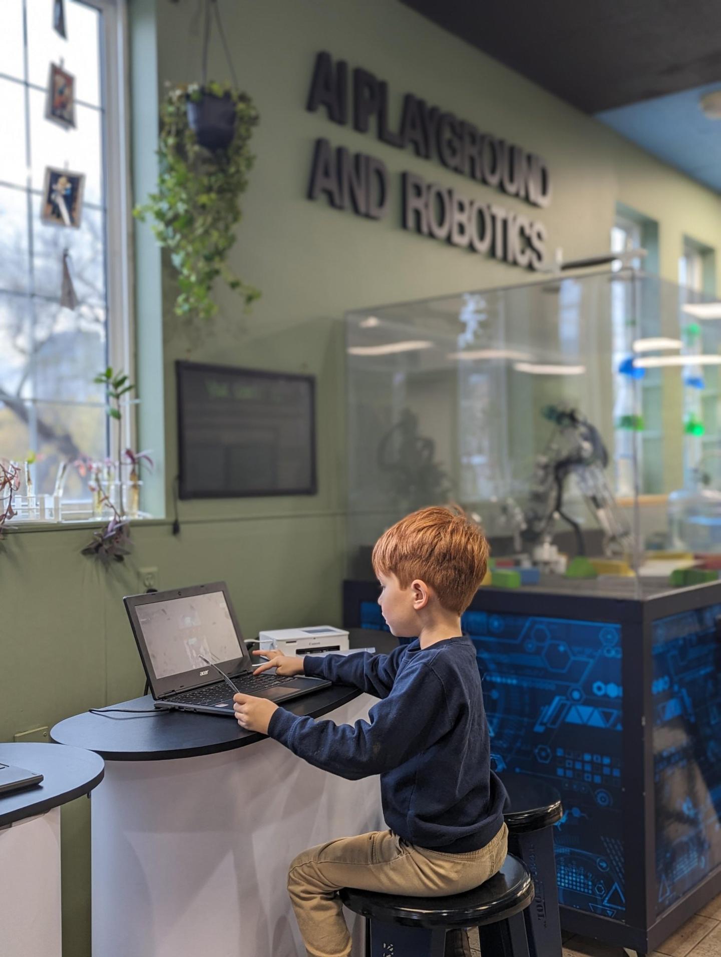 Young boy using a laptop in a robotics exhibit.