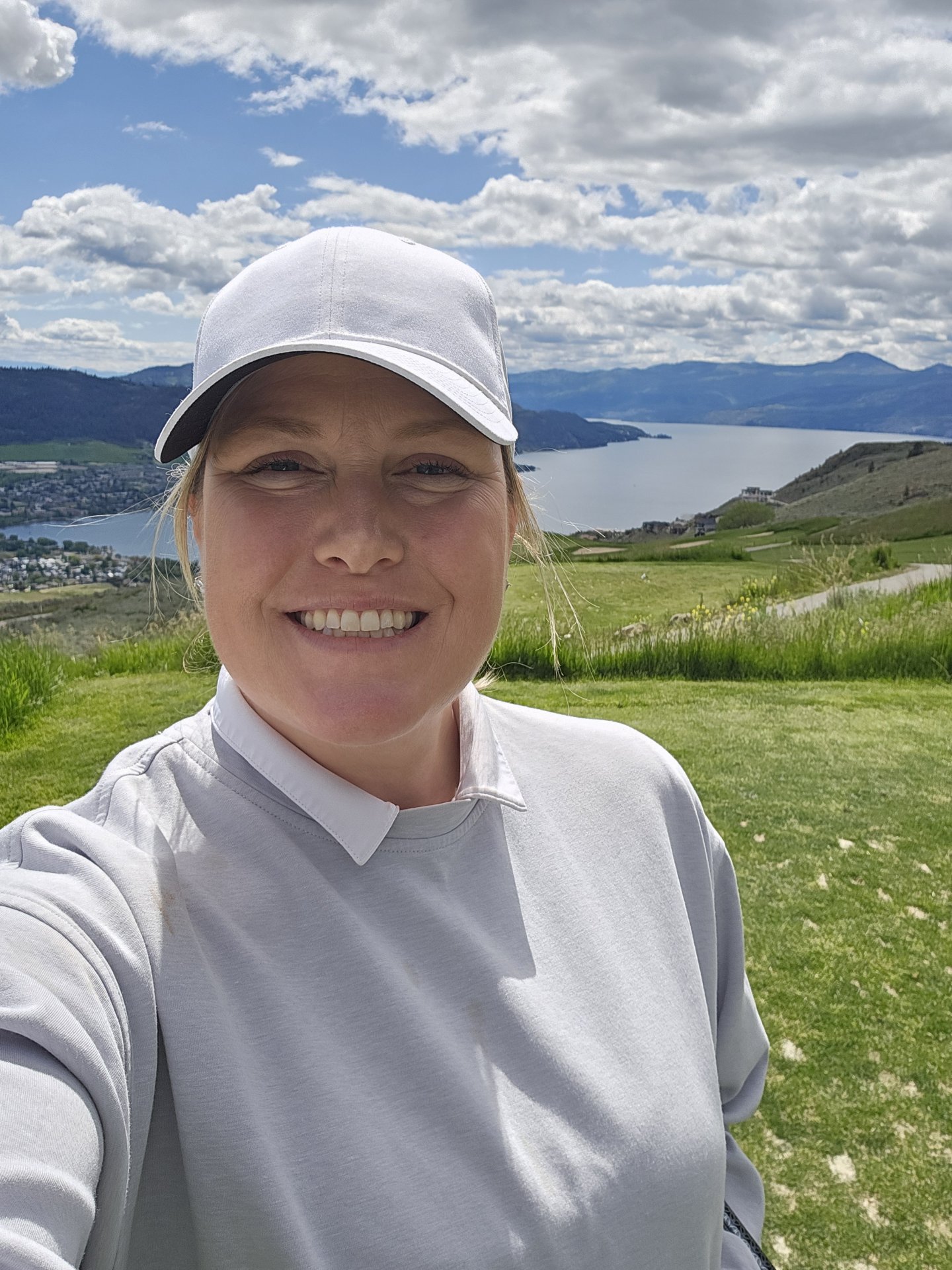Smiling woman in a white cap overlooking a lake and mountains.