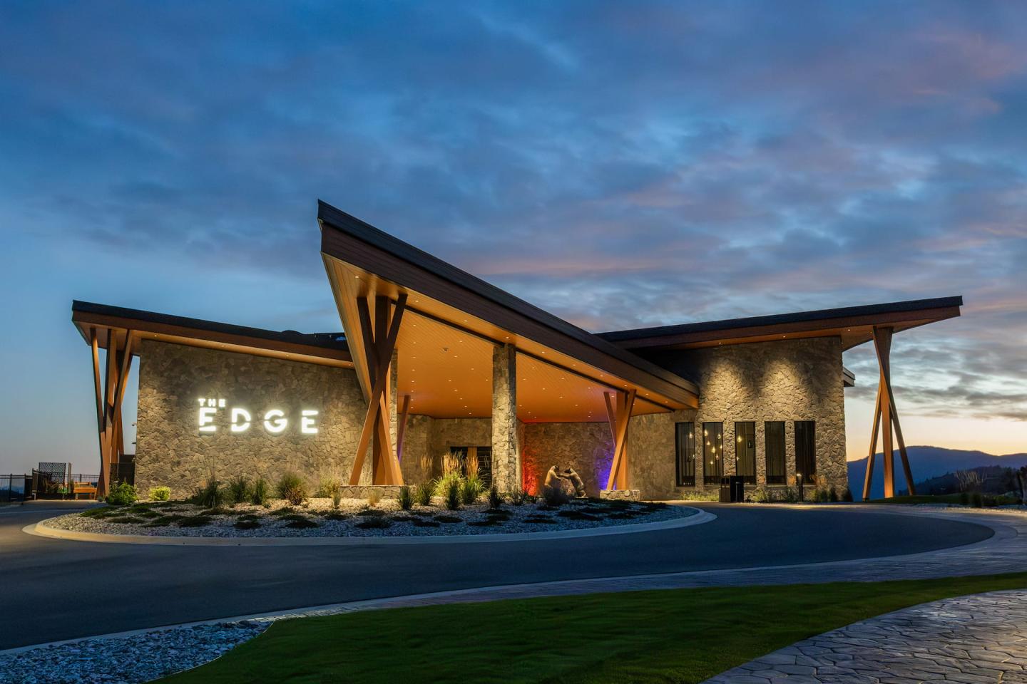 Modern lodge entrance at dusk with illuminated wooden beams and dramatic roof.