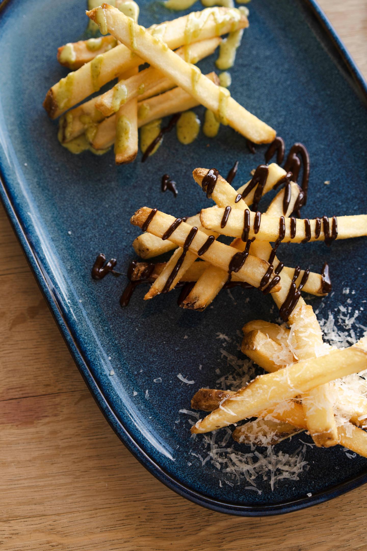Three gourmet frites with three different accompaniments on a blue plate.