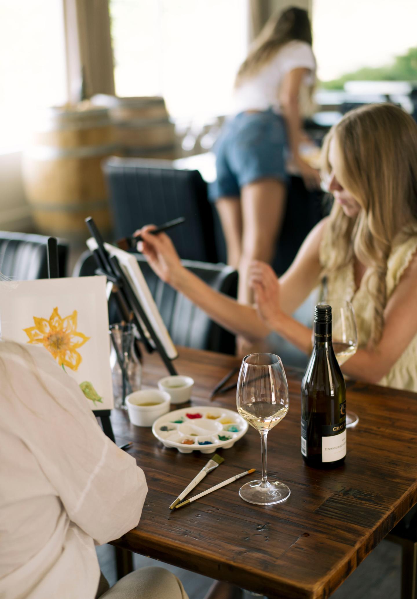 Two ladies painting flowers on a canvas. They are also enjoying a complimentary glass of Gray Monk wine. 