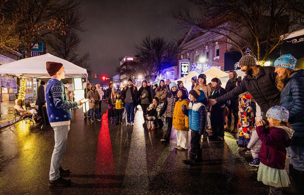 Crowd gathers along a wet, brightly lit street at night.
