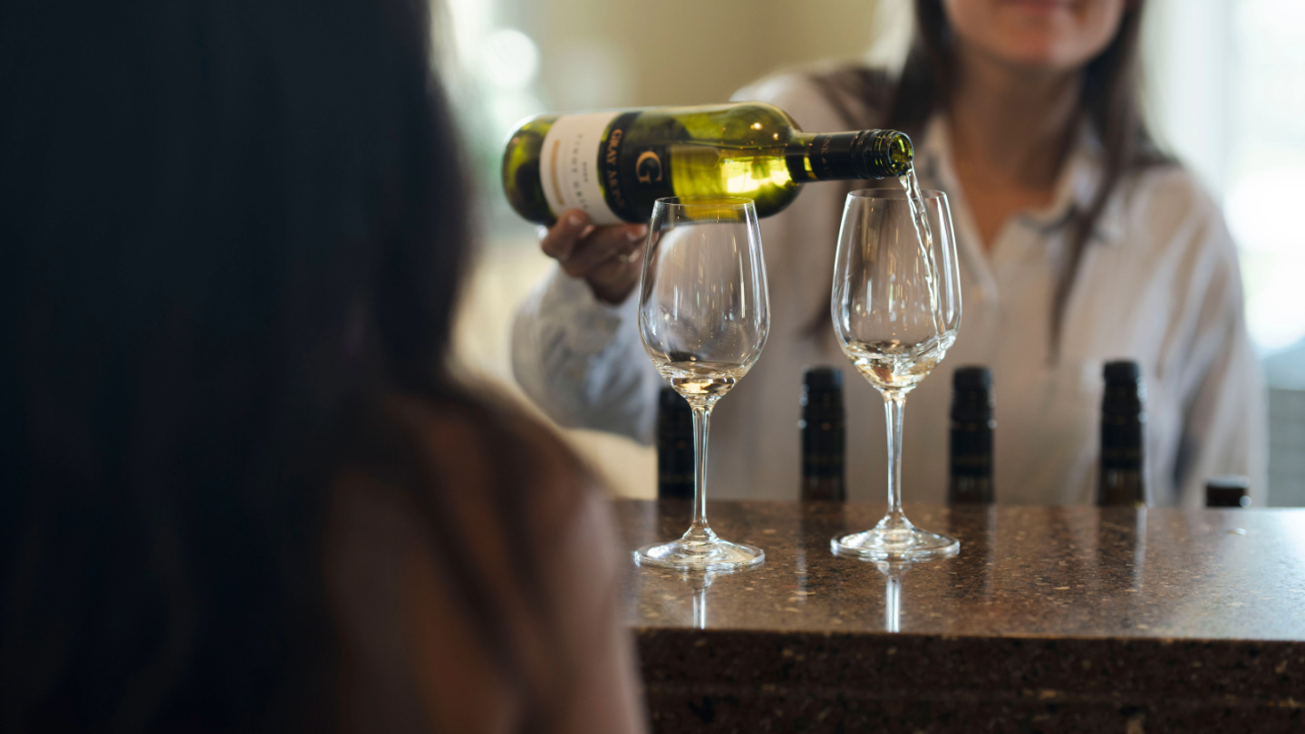 A woman pouring wine into a glass for a tasting.