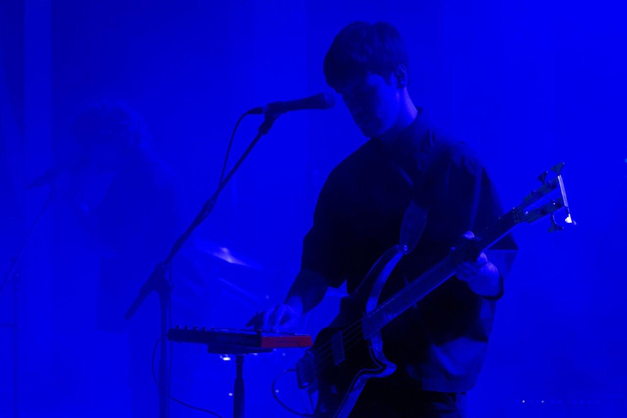 Guitarist performing onstage under deep blue lighting.