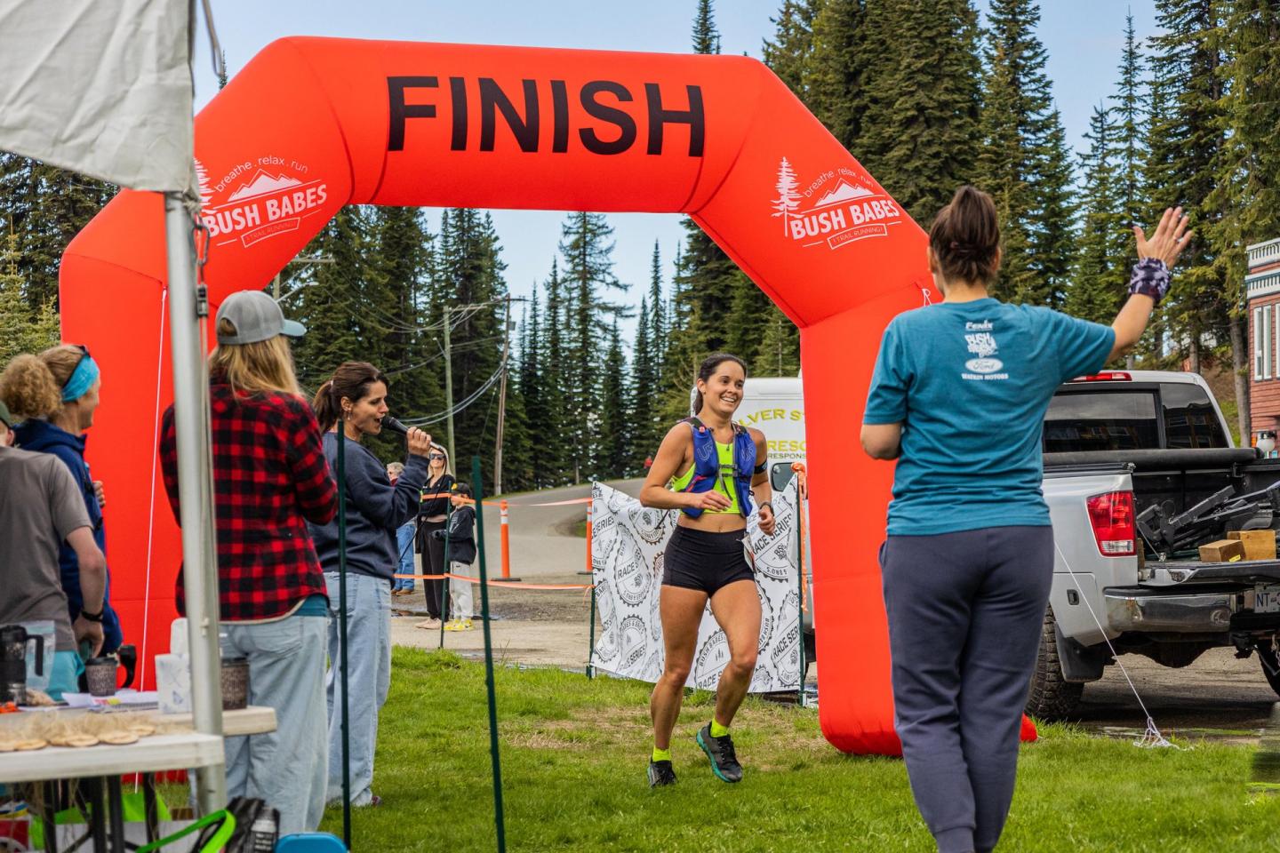 Runner crosses red FINISH arch at an outdoor race, with spectators nearby.